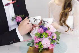 Para świętuje 4 rocznicę ślubu, trzymając kubki "Mr." i "Mrs." na tle bukietu kwiatów.