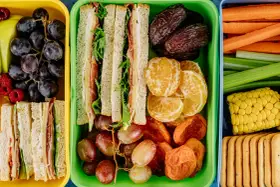 Kolorowe pojemniki pełne niskokaloryczne przekąski: kanapki, owoce, warzywa i ciastka. Idealne na zdrowy lunch.