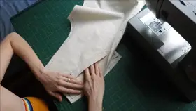 Mains travaillant sur un patron de couture, ajustant un tissu pour une poche raglan, à côté d'une machine à coudre Singer.