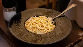 Pyszne cacio e pepe na czarnym talerzu, z widocznym młynkiem do pieprzu i solniczką w tle.