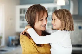 Uśmiechnięta mama i córka przytulają się, emanując ciepłem i bliskością. To kwintesencja rodzicielstwa bliskości.