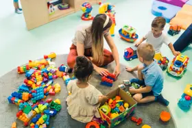 Dzieci bawią się klockami z opiekunką. Czy za żłobek się płaci? To pytanie zadają sobie rodzice, widząc radosne chwile swoich pociech.
