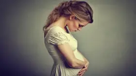 Kobieta w ciąży, zmartwiona, trzymająca się za brzuch. Wzdęcia w ciąży to częsty problem.