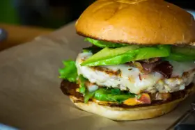 Pyszny hamburger z kurczakiem, awokado, serem i bekonem na brązowym papierze.
