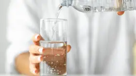 Eine Hand hält ein Glas, in das kohlensäurehaltiges Mineralwasser gegossen wird.