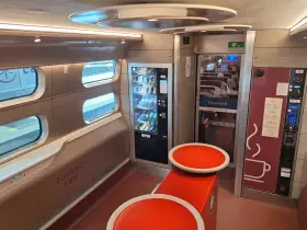 Interior of a Eurostar train from Amsterdam, featuring a cafe area with vending machines, seating, and windows looking out onto the tracks.