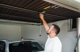 Mężczyzna sprawdza mechanizm bramy garażowej. Czy warto inwestować w garaże i miejsca postojowe przy obecnych cenach najmu?