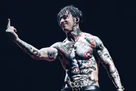Le chanteur de Falling In Reverse, Ronnie Radke, torse nu et couvert de tatouages colorés, lève le majeur sur scène.
