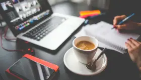 Tazza di caffè, laptop, smartphone e mani che scrivono su un quaderno. Questo è cosa significa da remoto: lavorare ovunque.