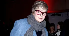 Karolina Korwin Piotrowska w okularach i niebieskim płaszczu, z szarym szalem na szyi.