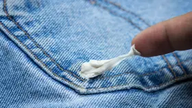 Ein Finger versucht, Kaugummi von Jeans zu entfernen. Der klebrige Kaugummi zieht sich zäh.