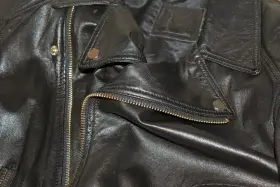 Dettaglio di una giacca in ecopelle nera con zip dorata e bottoni a pressione. Si pensa a come lavare giacca ecopelle in lavatrice.