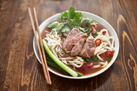 Un bol de soupe nouille de riz avec du bœuf, des germes de soja, des oignons verts et du piment rouge, prêt à être dégusté avec des baguettes.