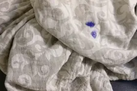 Niebieska plama po flamastrze na jasnej tkaninie z wzorem. Jak zmyć flamaster z ubrania?