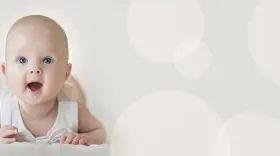 Uroczy 4 miesięczne dziecko z szeroko otwartymi oczami i buzią, leżące na brzuchu.