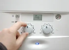 Dłoń reguluje pokrętłem pieca, przygotowując dom na nadchodzący sezon grzewczy. Na wyświetlaczu widnieje "110".