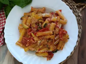 Piatto di pasta con zucchine e pomodorini, condita con formaggio grattugiato e basilico fresco.