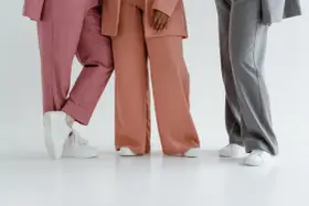 Trzy osoby w eleganckich stylizacjach. Jedna w różowych spodniach, druga w brzoskwiniowych, a trzecia w szarych. Zastanawiasz się, jaka marynarka do szarych spodni pasuje najlepiej?
