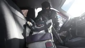 Złodziej w masce sięga po torbę w samochodzie. To jeden z rodzajów kradzieży, które mogą spotkać każdego.
