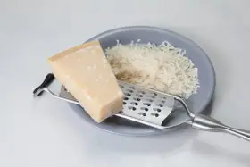 Kawałek parmezanu i starty ser na talerzu. Zastanawiasz się, czy parmezan można mrozić? Tak, można go mrozić, zachowuje wtedy smak.
