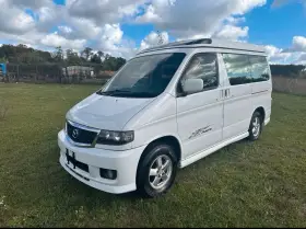 Biały van Mazda Bongo z podnoszonym dachem, zaparkowany na trawie.