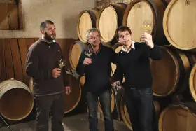 Trois hommes dégustent du vin dans la cave du domaine des Gandines, entourés de fûts de chêne.