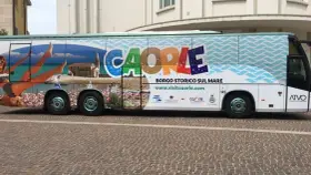 Bus turistico con grafica promozionale di Caorle, borgo storico sul mare. Immagini di spiaggia, mare e una donna in bikini.