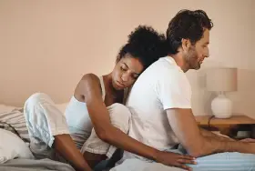 Un couple assis dos à dos sur un lit, l'air distant. On ne peut plus se parler sans s'engueuler.