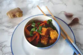 Pyszne dania z tofu z marchewką i szczypiorkiem, gotowe do jedzenia pałeczkami. Obok imbir i czosnek.