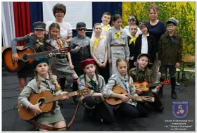Dzieci w strojach harcerskich grają na gitarach i mandolinie. To może być zapowiedź piosenki o harnasiu.