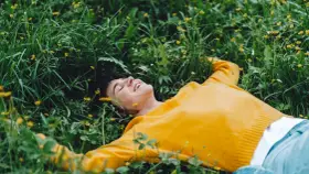 Persona sorridente sdraiata nell'erba verde con piccoli fiori gialli, godendosi un momento di digital detox.