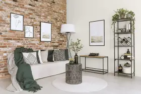 Nowoczesny salon z ceglaną ścianą, kanapą, stolikiem i regałem. Obrazy na ścianie tworzą wall of fame.