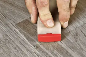 Fingrar använder en kil för att laga laminatgolv.