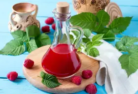 Malinowy ocet balsamiczny do sałatek, deserów, marynat. W butelce z korkiem, otoczony świeżymi malinami i liśćmi.