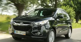 Czarny Hyundai ix35 jedzie drogą wśród zieleni.
