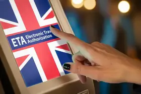 Dłoń dotyka ekranu z flagą Wielkiej Brytanii i napisem "ETA Electronic Travel Authorization". Czy do Londynu trzeba paszport? Sprawdź ETA.