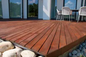 Belle terrasse en bois sur plot, avec des meubles de jardin et des rochers.