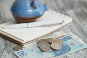 Świnka skarbonka, notatnik i długopis nad polskimi banknotami i monetami. Zastanawiasz się, ile wyniesie waloryzacja kapitału początkowego w 2025?