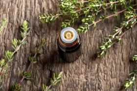 Flacone di olio essenziale di timo su legno rustico, circondato da rametti freschi. Un aiuto naturale per il raffreddore.