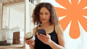 Kobieta sprawdza na telefonie, czy produkt ma dużo węglowodanów. Na półce stoją słoje z produktami.