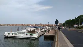 Un vaporetto attracca a Chioggia, con la città sullo sfondo e una strada trafficata.