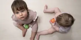 Dwa niemowlęta, jedno 9 miesięczne dziecko z niebieskimi oczami, bawi się zieloną piłeczką.