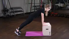 Kobieta wykonuje pompki na podwyższeniu, opierając dłonie na skrzyni.