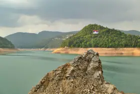 Serbska flaga na skale nad jeziorem. Krajobraz zachęca do podróży, a pytanie "czy Serbia jest bezpieczna dla turystów" wydaje się nie mieć znaczenia w obliczu tego spokoju.