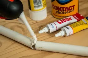 Aplikacja kleju butapren na pękniętą białą rurkę. W tle tubki z klejem i puszka "Contact Adhesive".