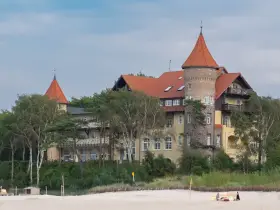 Elegancki hotel z wieżą i czerwonym dachem, otoczony drzewami, idealny na łeba atrakcje dla dorosłych.