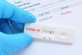 Rękawiczka ochronna trzyma test antygenowy COVID-19 z pozytywnym wynikiem.