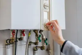 Main tenant ajuste le thermostat de sa chaudière à gaz. Une aide pour le changement de chaudière gaz est peut-être nécessaire.