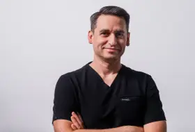 Portret mężczyzny w czarnym scrubie medycznym, ze skrzyżowanymi rękami.