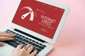 Schermo di un laptop con indicatore di velocità internet su sfondo rosso. Le mani digitano sulla tastiera, frustrati dall'internet lento.